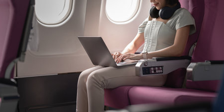 Joyful asian woman sits in the airplane and using mobile phone while go to travel