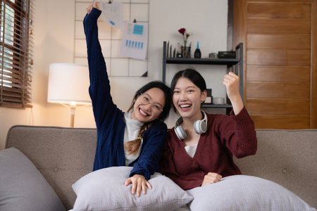 Two Young woman cheering together for sport on TV in cozy living room at homeの写真素材