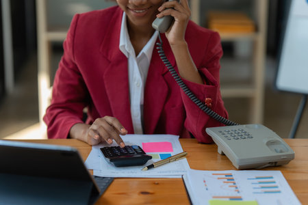 African American businesswoman using calculator and laptop for do math finance on wooden desk in office and business working background, tax, accounting, statistics and analytic research conceptの写真素材