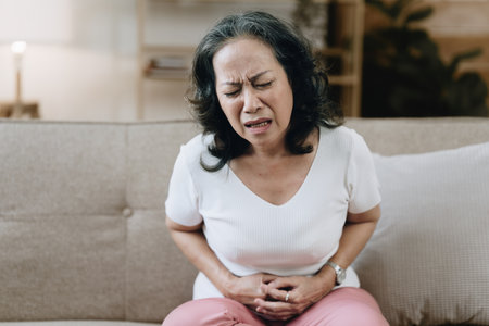 Asian woman in her eighties, exhausted and under stress, is at home with stomach pain