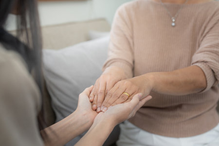 Loving adult daughter hugging older mother on couch at home, family enjoying tender moment together, young woman and mature mum or grandmother looking at each other, two generationsの写真素材