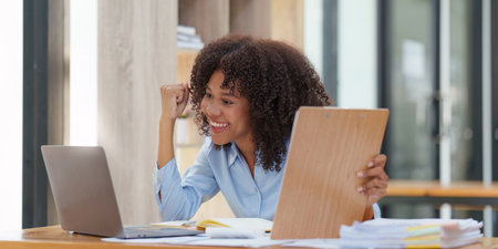 Black businesswoman work on laptop feel euphoric winning. Excited female triumph get good news from workの写真素材