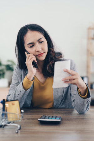Young Asian Woman checking bills, bank account balance, taxes and calculating expenses at homeの写真素材