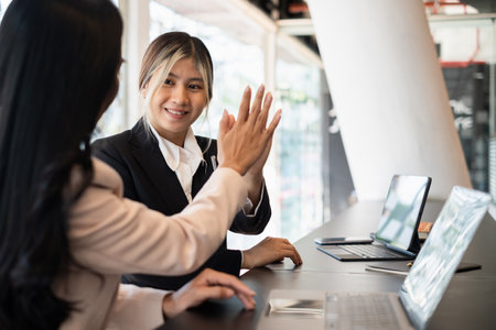 Asian businesswoman and her partners give each other high fives as they celebrate a successful team building project.の写真素材