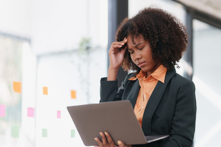 Portrait thoughtful confused young african american businesswoman looking at laptop. Stress while reading news, report or email. Online problem, finance mistake, troubleshootingの写真素材