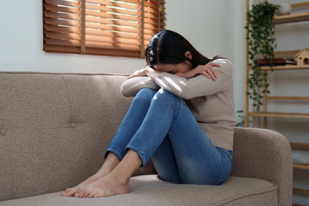 Unhappy female overworked and stressed sit at sofa at home. headache, depression feeling exhausted frustrated with bad news, failure at workの写真素材