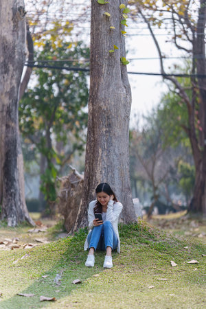Cheerful overjoyed woman happy and enjoying peaceful beautiful in park and using social media by smartphoneの写真素材