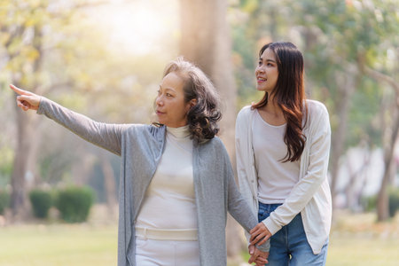 Adult daughter holding her elderly mother hand with love and walk togetherの写真素材