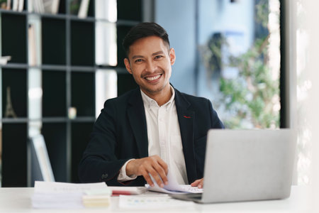 Smiling Asian Banker makes financial report and studies annual figures, analyzes profits. Accountant checks status of financialの写真素材
