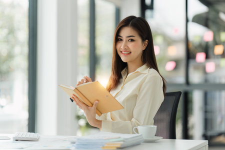 Beautiful Asian Banker or Accountant makes financial report and tax, analyzes profits. Accountant checks status of financialの写真素材