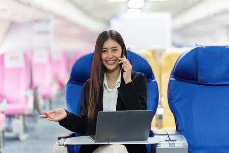 Beautiful Asian business woman chatting with client by mobile phone during flight. working, travel, business conceptの写真素材