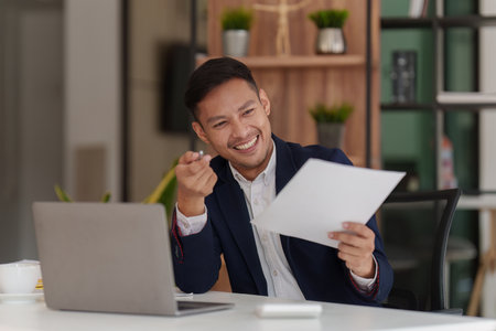 Smiling Asian Banker makes financial report and studies annual figures, analyzes profits. Accountant checks status of financialの写真素材
