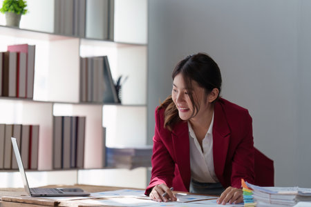 Smiling Asian Banker makes financial report and studies annual figures, analyzes profits. Accountant checks status of financialの写真素材