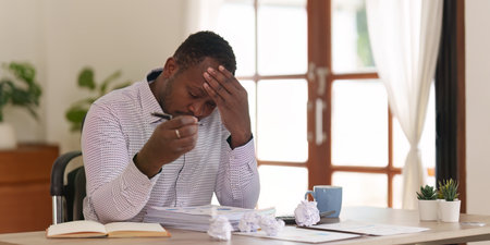 Tired American African business man in stress works with many paperwork document. migraine attack....