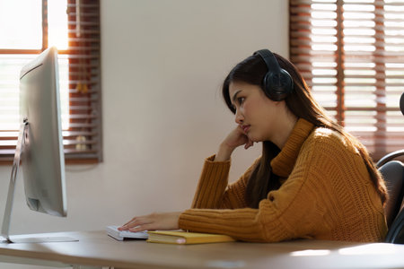 Online education, e-learning. Asian woman relaxing after studying using a laptop, listening to online lecture, taking notes, online study at homeの写真素材