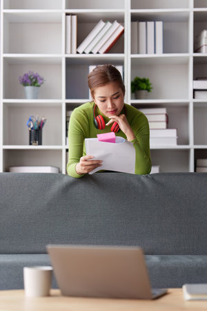 Woman sits on sofa at home, studying and analyze house bills and submitting tax forms.の写真素材