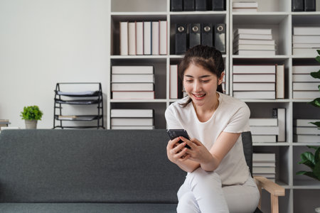 Young relaxed smiling pretty woman relaxing sitting on sofa at home. Female feeling joy enjoying with mobile phone on cozy couchの写真素材