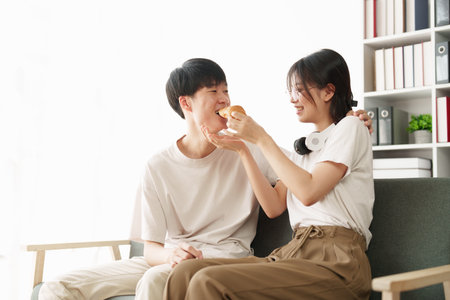 Beautiful asian couple in love and smiling sitting on sofa at morning. Romantic moment, relationships, family conceptの写真素材