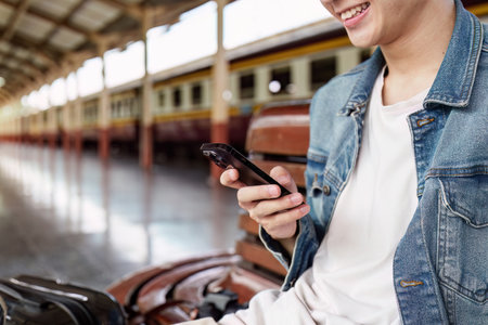 Asian Tourist person backpacker to travel at train station and using mobile phone. Tourism and travel in the summerの写真素材