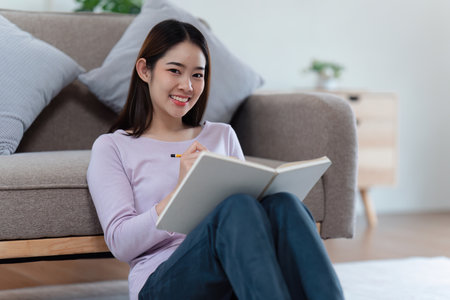 Online education, e-learning. Asian woman in stylish casual clothes, studying using a laptop, listening to online lecture, taking notes, online study at homeの写真素材
