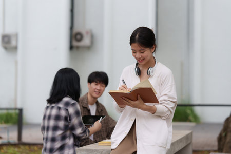 Beautiful young Asian woman college student with friends at outdoors. College student working on the college campus.の写真素材