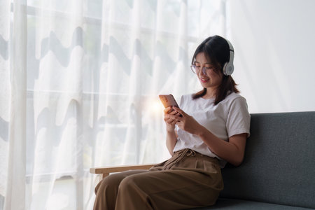 Young relaxed smiling pretty woman relaxing sitting on sofa at home. Female feeling joy enjoying with mobile phone on cozy couchの写真素材