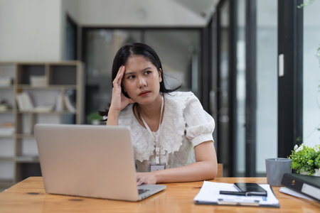 Stressed Financier a asian woman at works, uses a laptop, makes a report to a finance company. Accounting and financial conceptの写真素材