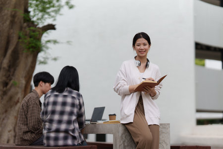 Beautiful young Asian woman college student with friends at outdoors. College student working on the college campus.の写真素材