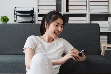 Young relaxed smiling pretty woman relaxing sitting on sofa at home. Female feeling joy enjoying with mobile phone on cozy couchの写真素材