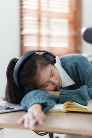 Online education, e-learning. Asian woman relaxing after studying using a laptop, listening to online lecture, taking notes, online study at homeの写真素材