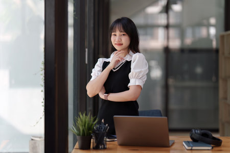 Online education, e-learning. Asian woman in stylish casual clothes, studying using a laptop, listening to online lecture, taking notes, online study at homeの写真素材