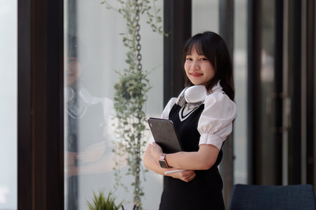 Online education, e-learning. Asian woman in stylish casual clothes, studying using a laptop, listening to online lecture, taking notes, online study at homeの写真素材