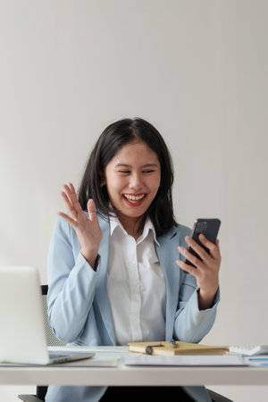 Smiling Asian Accountant person talking phone with client and makes financial report and studies annual figures, analyzes profitsの写真素材