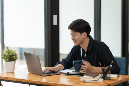 Young businessman drinking coffee and working using laptop and documentsの写真素材