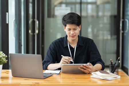 young Asian businessman using a digital tablet at a table in the officeの写真素材