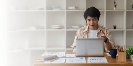 Young asian businessman connecting with his team online and using video call by laptop computerの写真素材