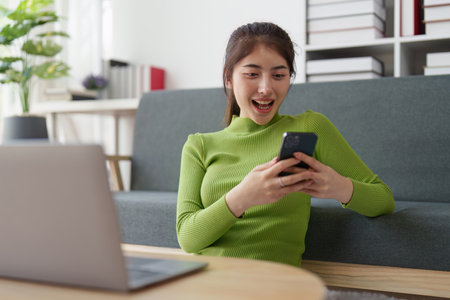Young asian relaxed smiling pretty woman relaxing with mobile phone at home. Female feeling joy enjoying with mobile phone on cozy couchの写真素材