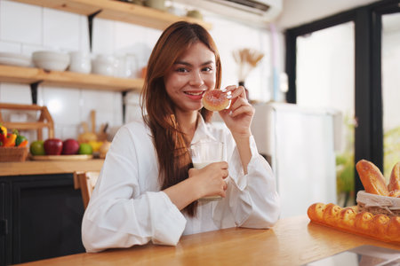 Portrait of a young cheerful asian woman drinking milk in kitchen room with healthy raw food....