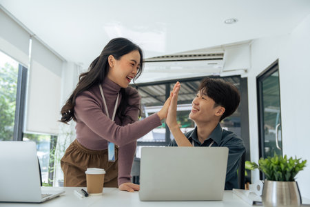 happy Asian female office worker gives high fives to a male colleague, celebrating project successの写真素材