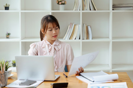employee with paper work inside office, female financier worker thinks about contracts and reports with charts and graphs, successful woman uses laptop at work.の写真素材