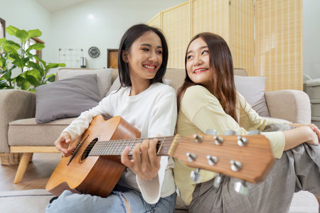LGBTQIA lesbian gay couple playing guitar and singing with romantic feelings at homeの写真素材