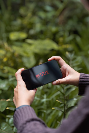 CHIANG MAI, THAILAND - AUG 08, 2023 : Woman holds iPhone 14 Pro max with red Netflix brand logo on...