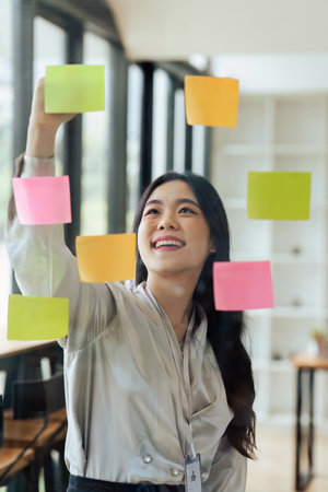 Through glass view of businesswoman analyzing process schedule, planning tasks on sticky papers