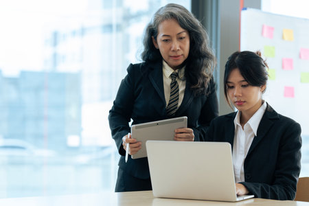 Two diverse financial assistant working on laptop while senior professional standing and giving investment adviseの写真素材