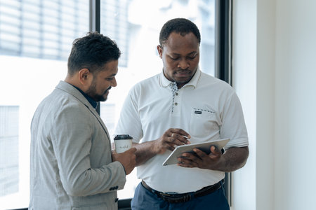 Two happy diverse coworker discussing report financial on tablet, working on project together