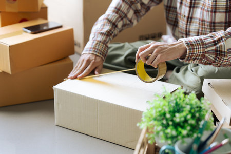Young man sealing big cardboard box with tape for moving to new home. relocation conceptの写真素材