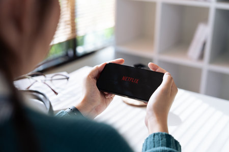 CHIANG MAI, THAILAND - Sept 01, 2023 : Woman holds iPhone 14 Pro max with red Netflix brand logo on its screen in the evening. Netflix is a global video streaming service.のeditorial素材