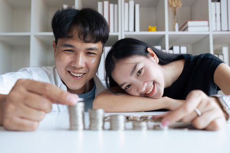 Happy Young Couple sitting with stacks of golden coins over table at homeの写真素材