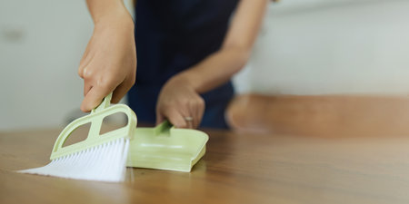 housekeeper woman with green light broom and dustpan sweeping remove dust on table at home