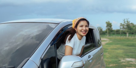 Smiling female driving vehicle on the road on a bright day. Sticking her head out the windshieldの写真素材